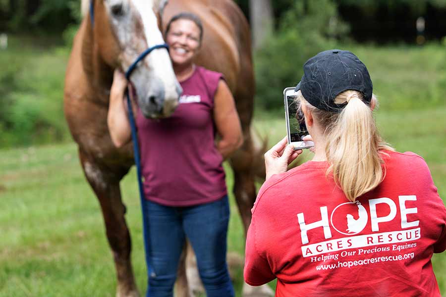 Becky takes a photo of Tracey standing with Maci, one of the Belgian mares. Photo by Jess Schaer, Schaer Studios