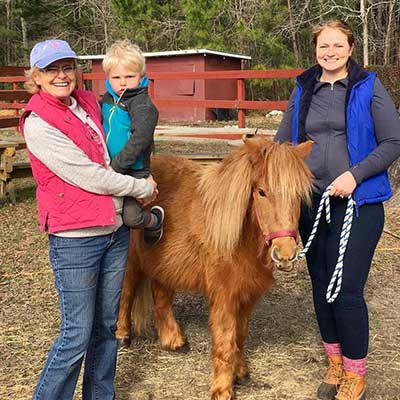 Red, a shetland pony, standing with his new adoptive family.